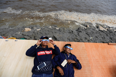 Boys wearing special protective glasses lie on a wooden board as they observe the annular solar eclipse in Siak, Riau province, Indonesia
