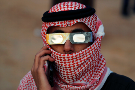 A Saudi man in red-and-white check head wrap watches the eclipse