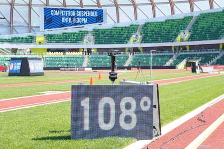 Sign displaying temperature of 108 degrees sits on athletic field below sign reading &quot;
