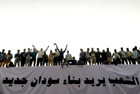 Sudanese demonstrators stand next to a banner reading in Arabic &quot;People want to build new Sudan&quot; as they chant slogans during a protest rally demanding Sudanese President Omar Al-Bashir to step down, outside Defence Ministry in Khartoum, Sudan April 9, 2019.