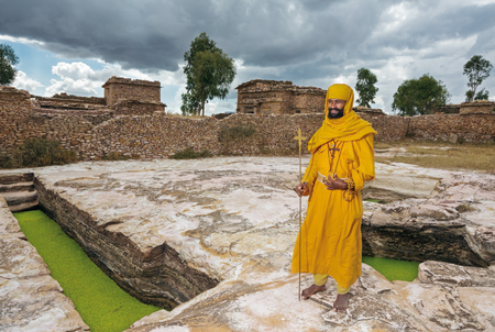 Monk Mikael, holding a pilgrim’s cross, stands by two of the hand-cut rock cisterns that capture enough water during the rains to last the community the entire year.