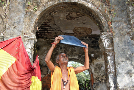 A Hindu priest watches a partial solar eclipse through exposed x-ray film outside a temple in Agartala, India