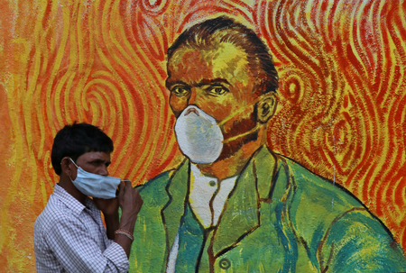 A man walks past a wall mural depicting Van Gogh&#039;s self-portrait but with a mask in Mumbai.