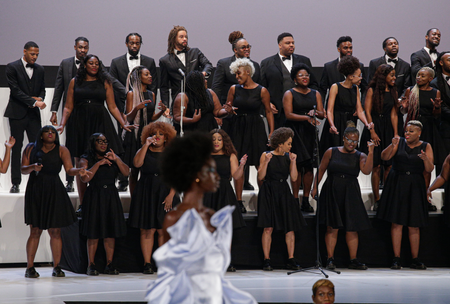 A choir of women in black dresses and men in black tuxes sing and dance during the Pyer Moss show