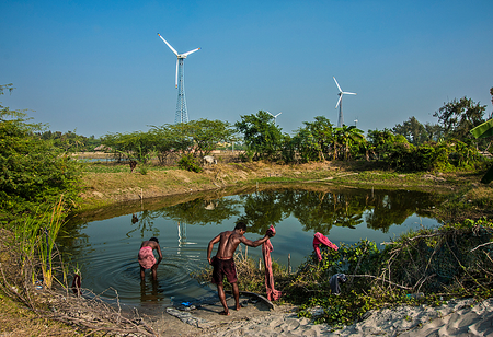 Power source in rural life, two men by a pond, washing and bathing by three windmills generating power.