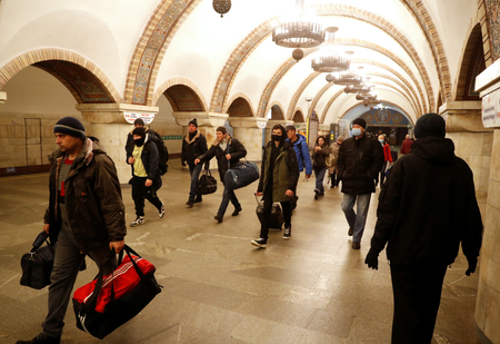 many people walk in an underground subway station corridor with arched walls and chandeliers hanging from the ceiling.