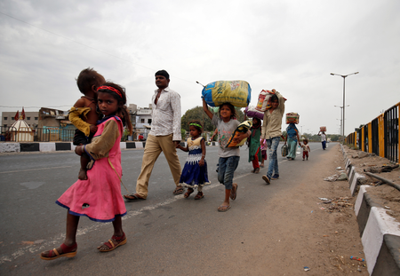 Migrant workers walk with their children as they look out for transport to return to their villages, in Ahmedabad