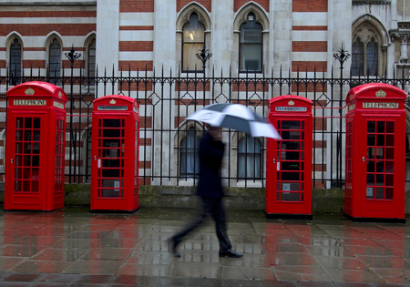 A man shelters under an umbrella as he walks past red telephone boxes in central London April 17, 2012. REUTERS/Olivia Harris (BRITAIN - Tags: CITYSPACE SOCIETY BUSINESS TELECOMS) - RTR30UWV