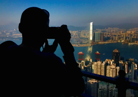 A visitor to Victoria Peak takes photographs of buildings on Hong Kong Island and Kowloon
