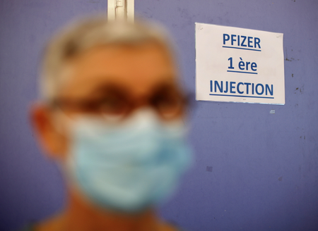 A woman wearing a protective face mask stands by a sign reading &quot;Pfizer first injection&quot; in a vaccination center in Antibes as part of the coronavirus disease vaccination campaign in France