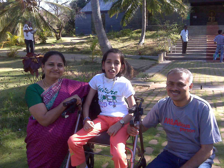 Nidhi Shirol on a wheelchair with her parents on either side in a park