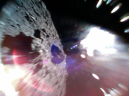 Image captured by Rover-1B on September 21 at around 13:07 JST. This color image was taken immediately after separation from the spacecraft. The surface of Ryugu is in the lower right. The coloured blur in the top left is due to the reflection of sunlight when the image was taken.