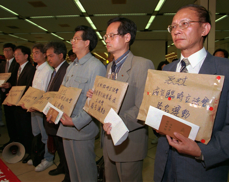 Seven members of a coalition to oppose a Beijing-appointed provisional legislature show 60,000 signatures in brown envelopes to journalists at Hong Kong&#039;s Kai Tak Airport Monday, July 1, 1996. They flew to Beijing with a petition, calling on the Chinese government to allow direct elections in Hong Kong after it returns to Chinese rule in 1997. (AP Photo/Vincent Yu)