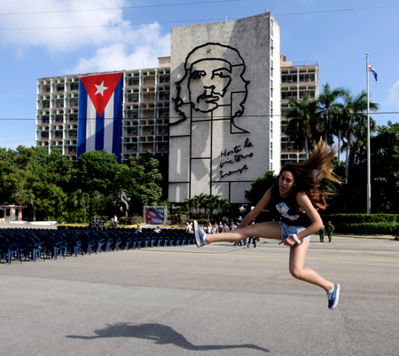 Carolina, a tourist from Chile, jumps while having her picture taken by a friend before a tribute to revolutionary leader Che Guevara in front of the Cuban Interior Ministry (MININT) in Havana&#039;s Revolution Square October 8, 2013. Forty-six years after he was captured by soldiers in a Bolivian jungle and executed the next day, the Argentine-born Ernesto Guevara De La Serna, AKA, &#039;Che&#039;, is still a national hero in Cuba where he joined Fidel Castro in an armed uprising that ousted a U.S. backed dictator in 1959. Tuesday will be Guevara&#039;s 46th death anniversary. The words on the building read: &quot;Onward to victory, always&quot;.