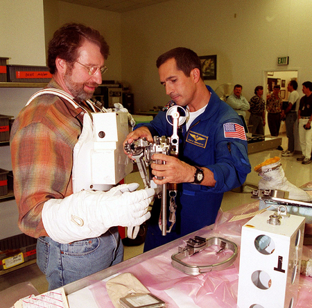 KENNEDY SPACE CENTER, FLA. -- Astronaut John Herrington (right) helps Norm Abram try on a tool carrier used in space. Abram is the master carpenter on television’s &quot;This Old House.&quot; He is at KSC to film an episode of the series