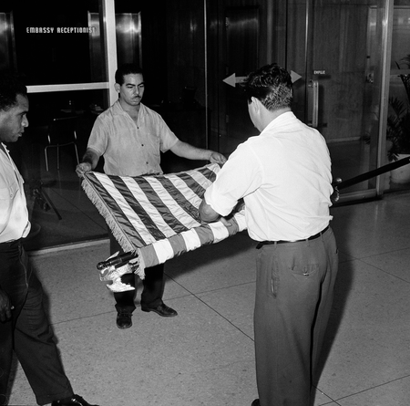 FILE - This Jan. 7, 1961 file photo shows unidentified U.S. embassy employees rolling up a U.S. flag as the embassy transfers American affairs to the Swiss government, in Havana, Cuba. The U.S. Interests Section is poised to be transformed into a full embassy, which would include such symbolic measures such as raising the American flag on the Malecon, after the U.S. and Cuba announced on Dec. 17, 2014 they are re-establishing full diplomatic relations.