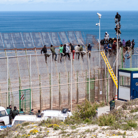 African migrants sit on top of a border fence covered in razor wire between Morocco and Spain&#039;s north African enclave of Melilla during their latest attempt to cross into Spanish territory, April 3, 2014. Spain has more than doubled the strength of security forces at Melilla, after about 500 people stormed its fences in the biggest border rush for years earlier this month. Immigrants from all over Africa regularly dare the razor-wire fences of Spanish enclaves Ceuta and Melilla, which are surrounded by Moroccan territory and sea.