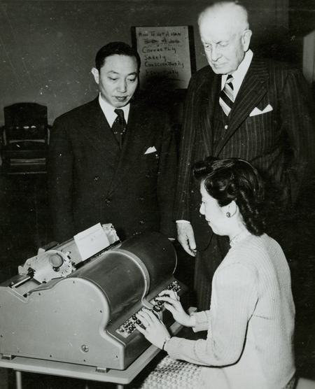 A woman types on Kao&#039;s Chinese electric typewriter, as IBM president Thomas J. Watson looks on.