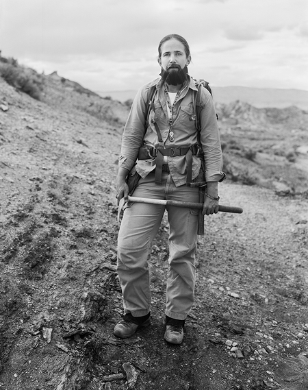Ellen Currano stands in the field wearing a beard in addition to her usual field work gear.