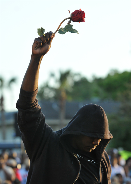 FILE - In this March 22, 2012 file photo James Gilchrist of Orlando, Fla., wearing a hoodie and holding a rose, attends a rally for Trayvon Martin in Sanford, Fla. Martin was shot by George Zimmerman, who claimed self-defense, as he patrolled a gated community in Florida. Though he was not a sworn police officer, his case raised some of the same questions in the wake of the killing of 18-year old Michael Brown in Missouri about the role race might pay in the killings of young black men by people in positions of authority. (AP Photo/Roberto Gonzalez, File)