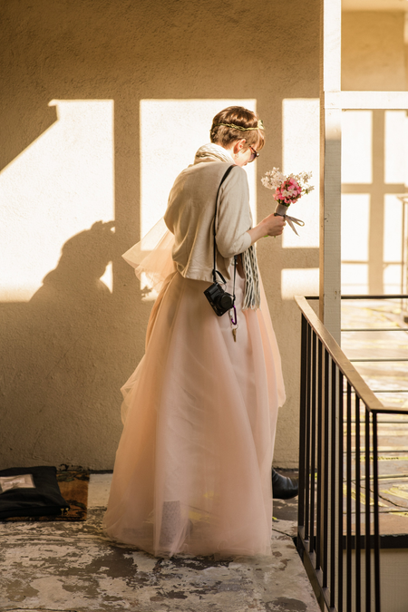 A photo of Christie heading out of their apartment in her wedding dress, bouquet in hand.