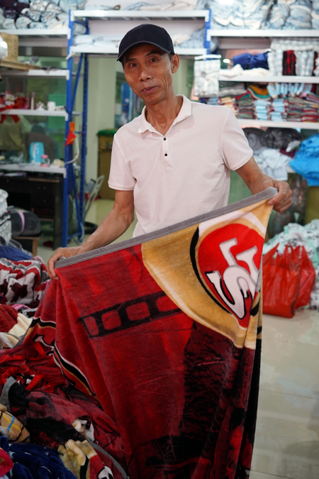 Changhe Zhou folds a blanket at his linen shop in Khorgos ICBC.