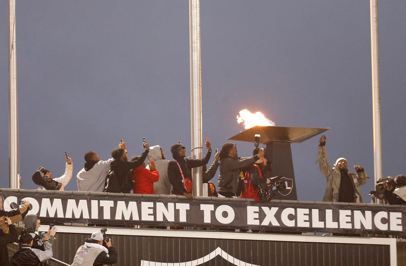 Oakland Raiders running back Marshawn Lynch, right, lights a ceremonial torch for former team owner Al Davis before an NFL football game between the Raiders and the Denver Broncos in Oakland, Calif., Monday, Dec. 24, 2018.