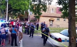 Residents in the Humboldt Park neighborhood on Chicago’s West Side gather around as officers remove a car from a crime scene with the bodies of deceased victims still inside. YouTube screenshot