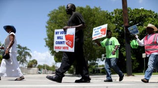 Voters hold up signs as they walk to an early-voting site in Miami on Aug. 11, 2014, to cast their ballots.Joe Raedle/Getty Images
