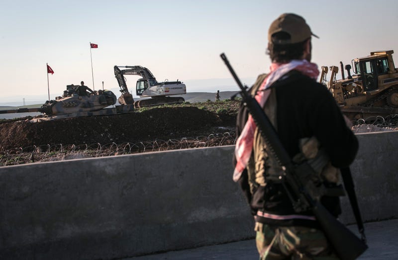 A Syrian Kurdish militia member of YPG patrols near a Turkish army tank as Turks work to build a new Ottoman tomb in the background in Esme village in Aleppo province, Syria, Sunday, Feb. 22, 2015. Turkey launched an overnight military operation into neighboring Syria to evacuate troops guarding an Ottoman tomb and to move the crypt to a new location, Turkish Prime Minister Ahmet Davutoglu said Sunday. Davutoglu said they plan to build a new Ottoman tomb in Esme village, close to Turkey-Syria border. (AP Photo/Mursel Coban, Depo Photos)