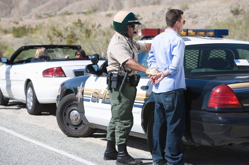 A man being arrested by police, who is arresting him outside his vehicle