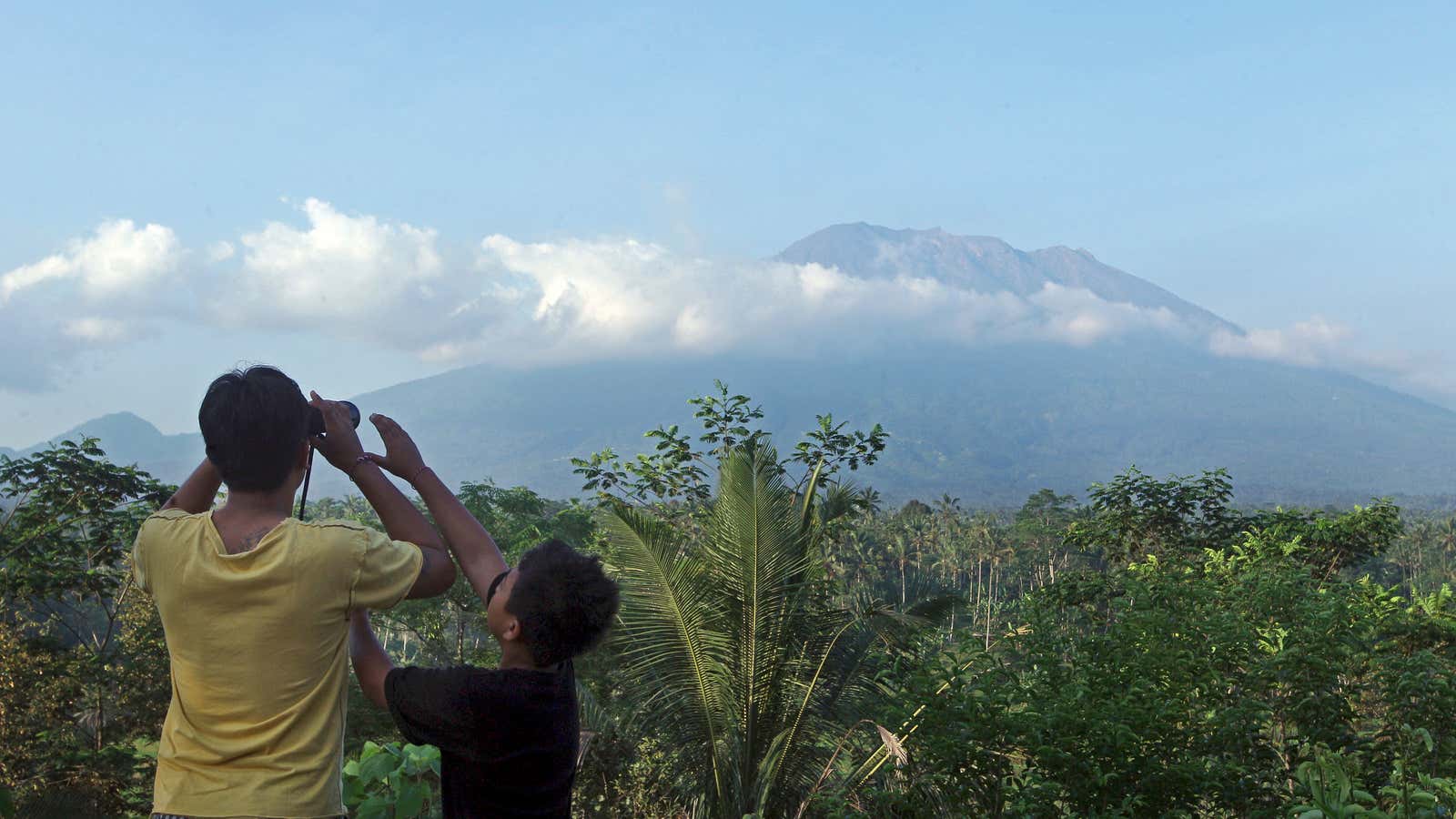 A man observes the Mount Agung with binoculars at a viewing point in Bali, Indonesia, Wednesday, Sept. 20, 2017. Officials have more than doubled the size of evacuation zone around the Mount Agung volcano o the tourist island of Bali and raised its alert level for the second time in less than a week. (AP Photo/Firdia Lisnawati)