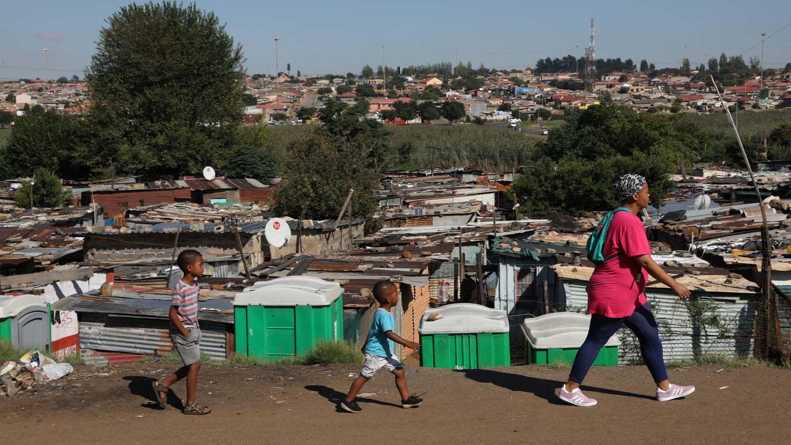 A mother and her children walk past public toilets at an informal settlement in Kliptown, Soweto, South Africa, Mar. 19, 2020.