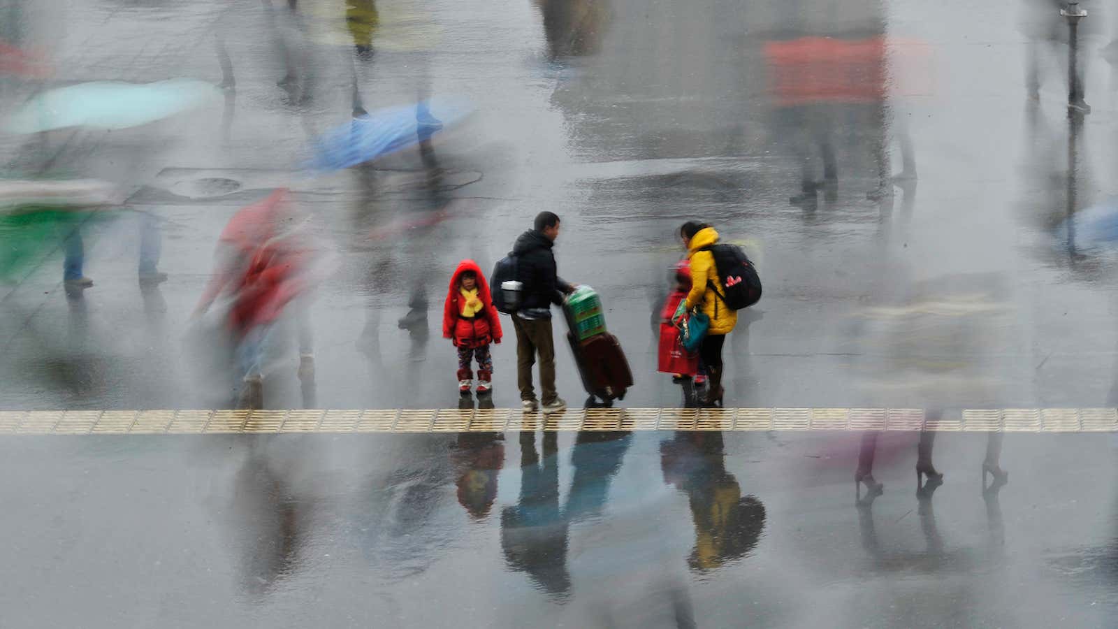 A long exposure photo shows a family standing under the rain outside a railway station in Hefei, Anhui province, February 6, 2014. According to Xinhua…