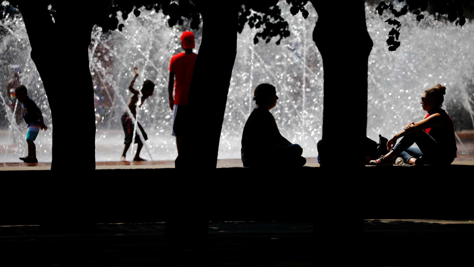 People sit in the shade and cool off in a fountain during a summer heat wave in Boston, Massachusetts, U.S., July 2, 2018.   REUTERS/Brian Snyder – RC142ED51E00