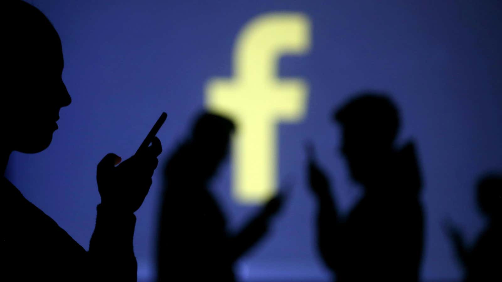 Silhouettes of mobile users are seen next to a screen projection of Facebook logo in this picture illustration taken March 28, 2018