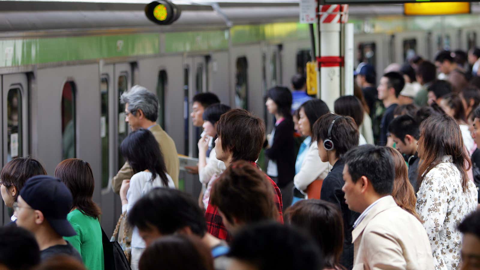 A crowd of people step forward as a train arrives at a station in Tokyo.
