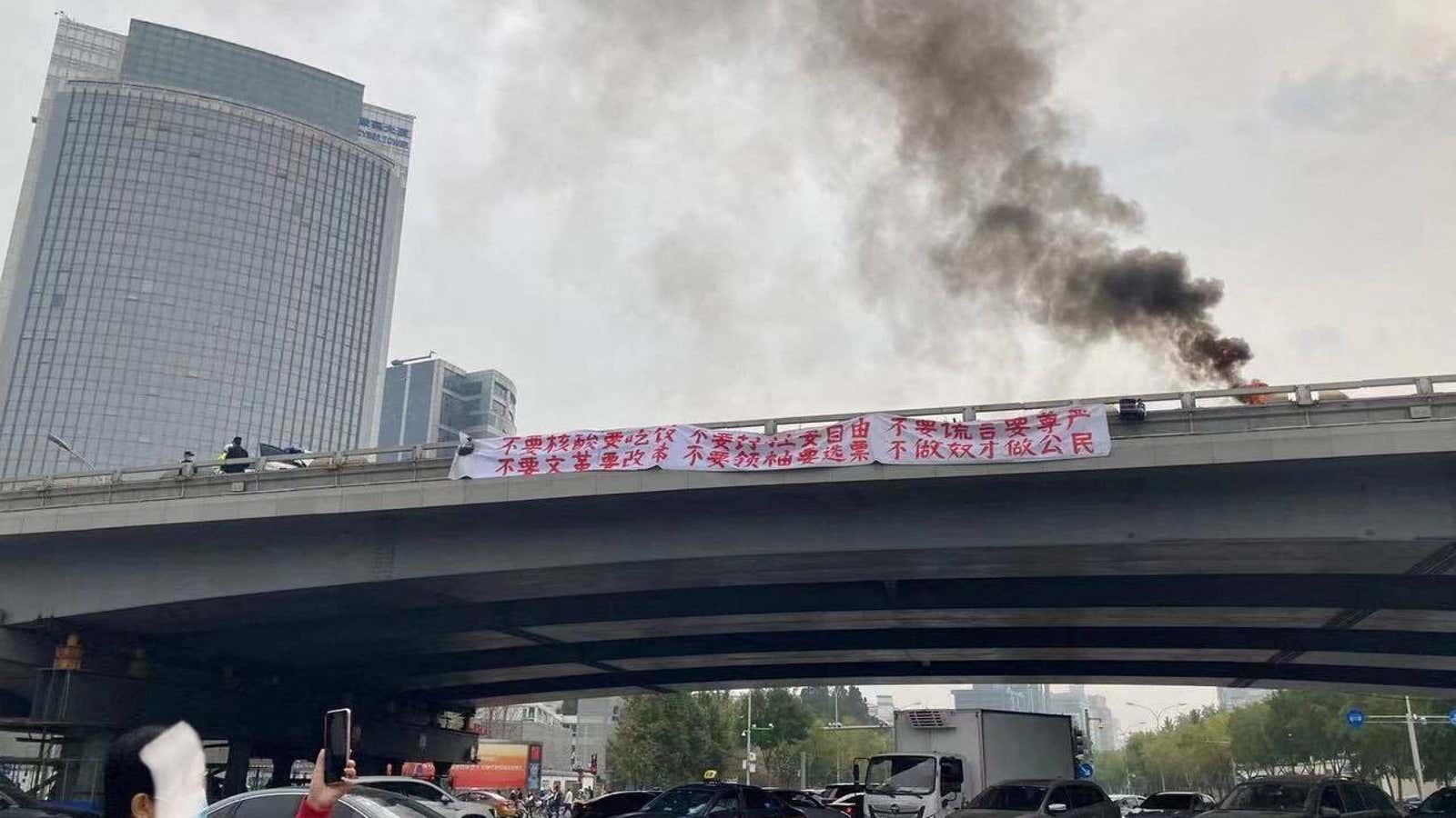 Smoke rises above a banner with a protest message that hangs off Sitong Bridge, Beijing, China on October 13, 2022.
