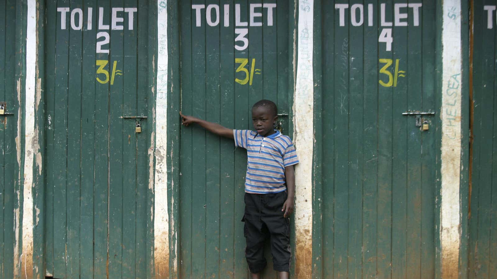 A boy stands next to a public bathroom in Nairobi’s slum, Kibera.