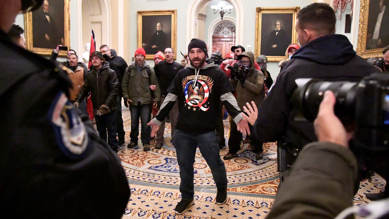 A supporter of president Donald Trump, wearing a QAnon shirt, confronts police in the US Capitol after breaching security defenses.