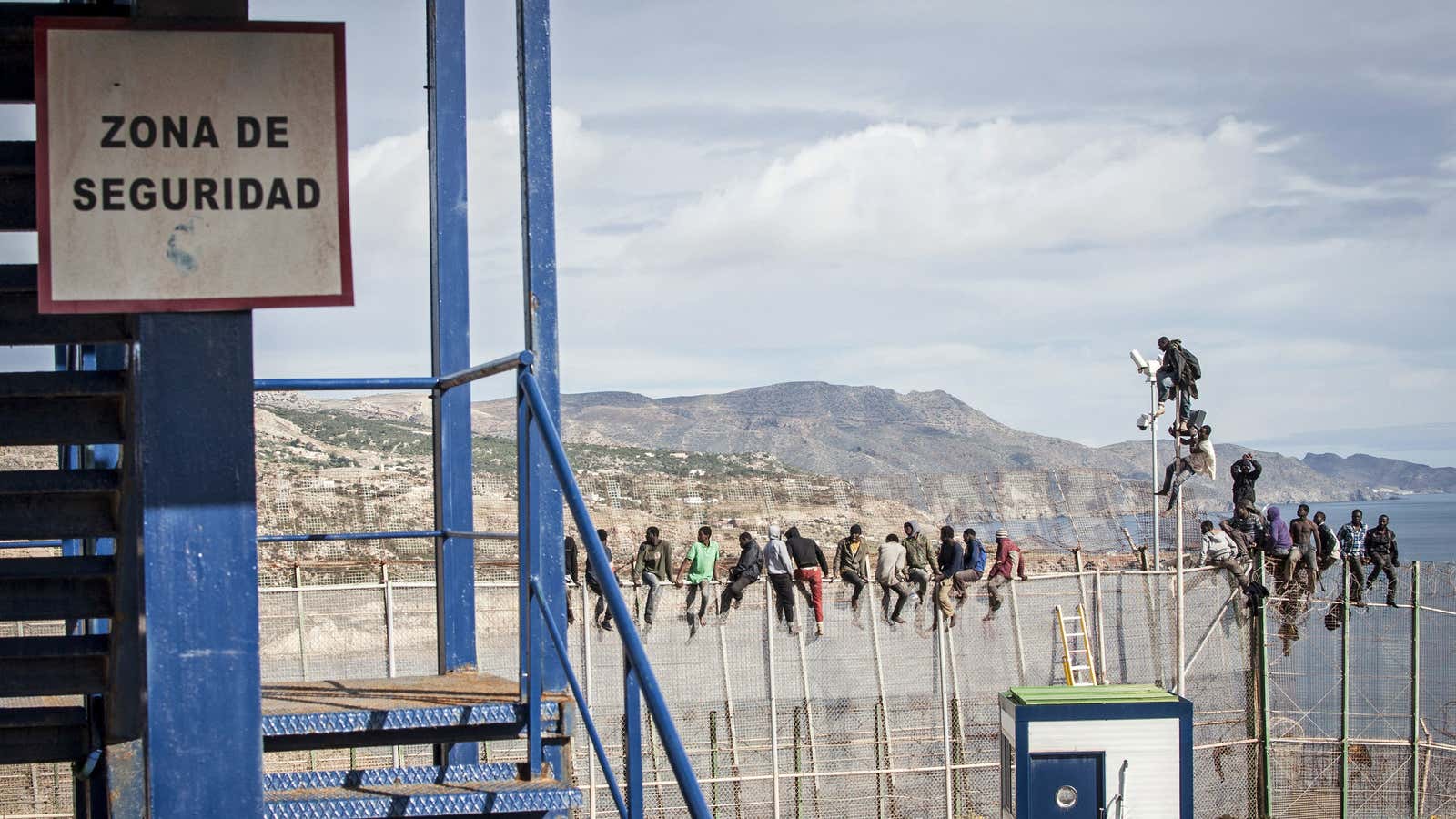 Migrants sit on top of a border fence in Melilla.