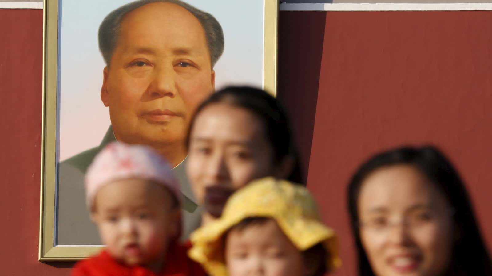 Two women and their babies pose for photographs in front of the giant portrait of late Chinese chairman Mao Zedong on the Tiananmen Gate in…
