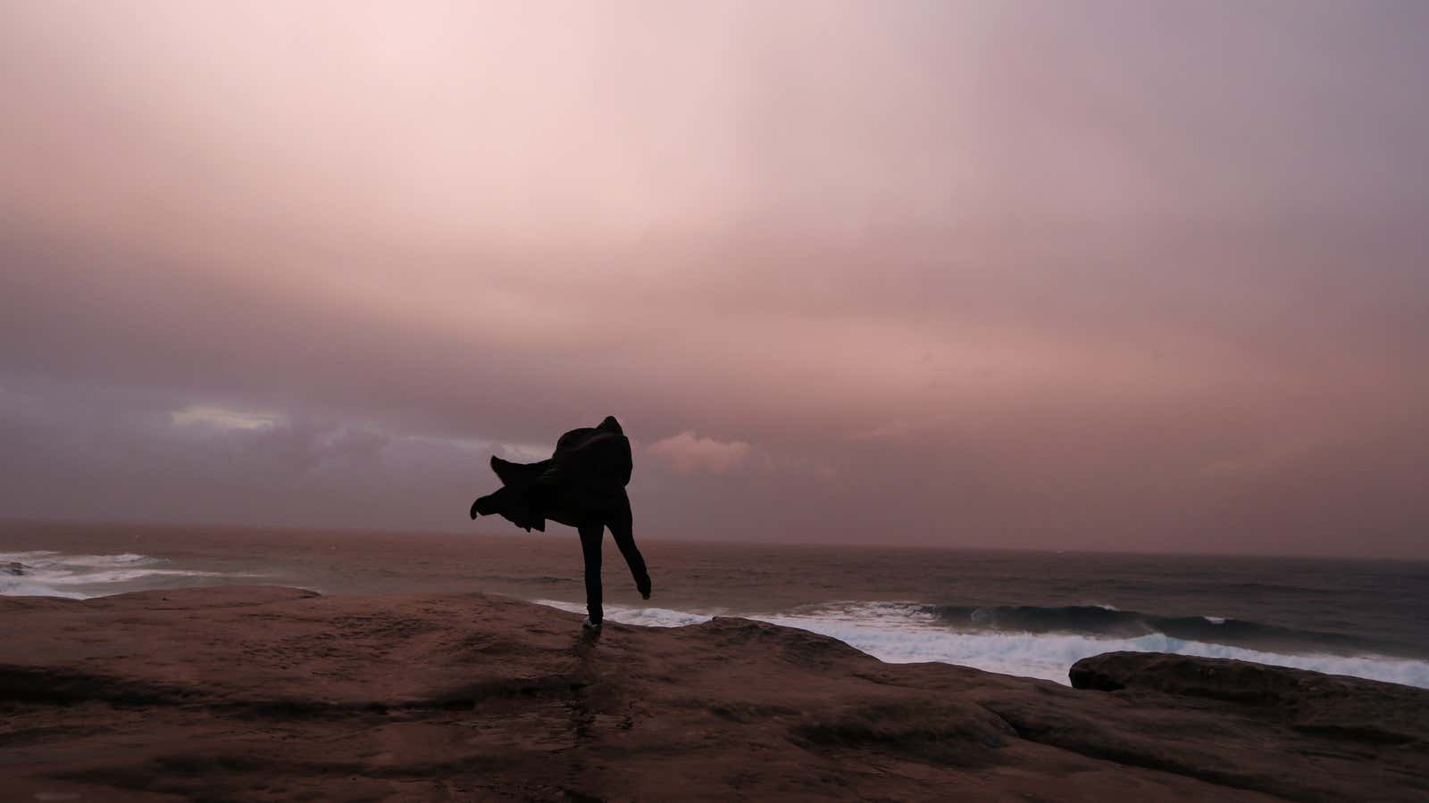 A woman plays on the edge of a cliff on a rainy winter afternoon at Bronte beach in Sydney August 8, 2013. REUTERS/Daniel Munoz (AUSTRALIA – Tags: SOCIETY ENVIRONMENT TPX IMAGES OF THE DAY) – GM1E9881CMI02