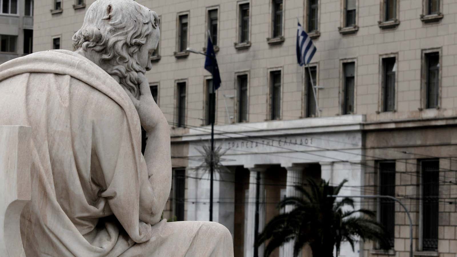 A statue of the ancient Greek philosopher Socrates is pictured with the headquarter of the central Bank of Greece in the background in Athens on…