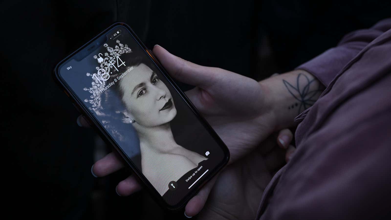 A person holds a smartphone with an image of Queen Elizabeth II as their screensaver. 