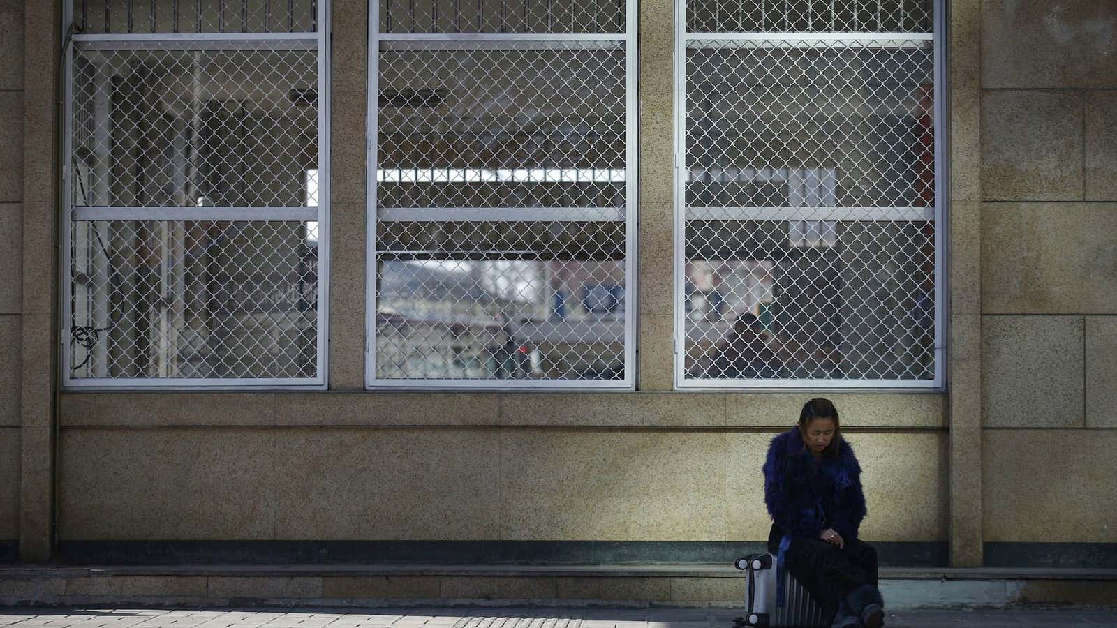 A woman sits outside an empty Beijing railway station.