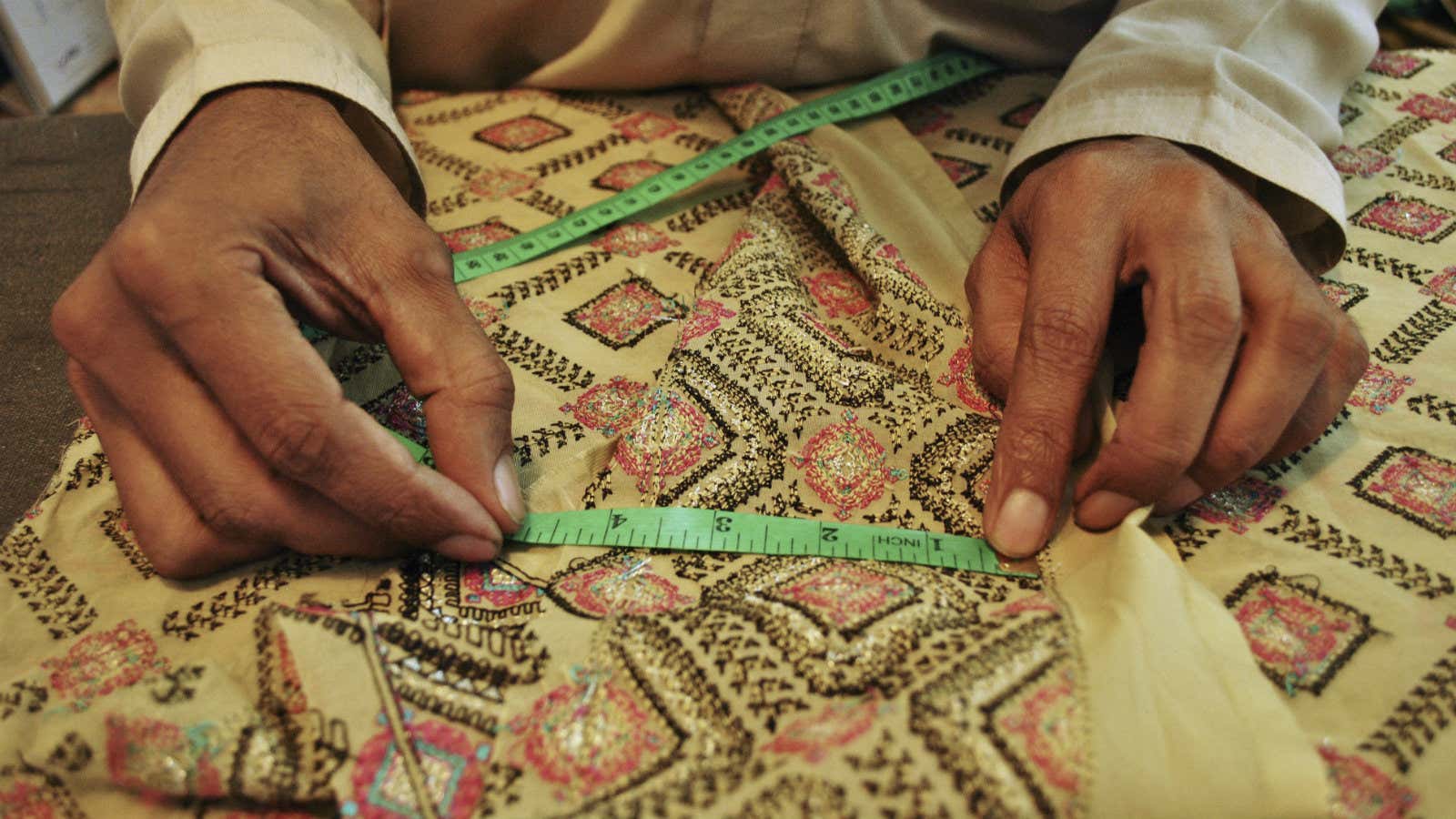 A senior master tailor at Needles Tailoring makes measurements before cutting fabric in Mardan, Pakistan.