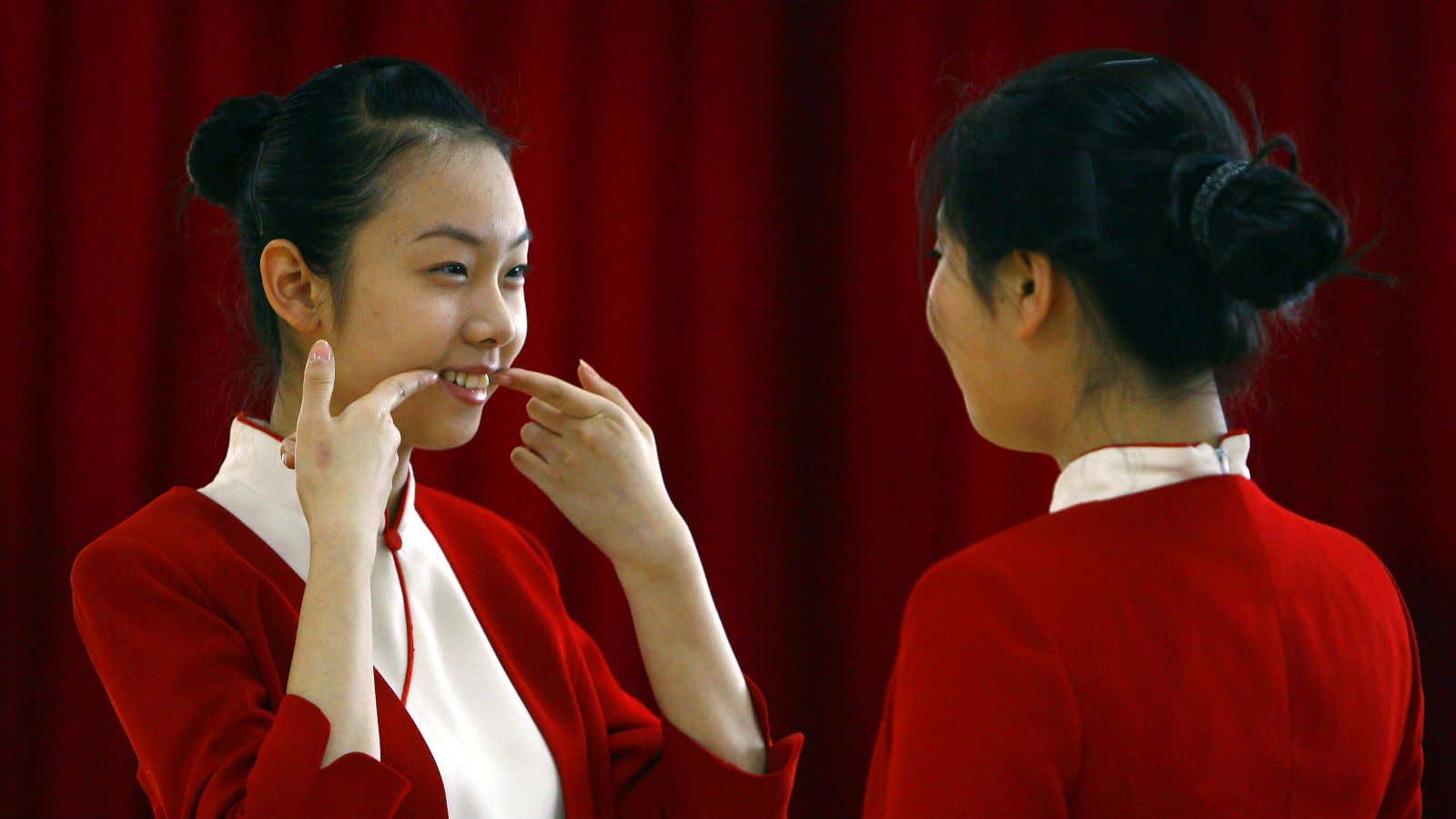 A student shows another how to smile during an etiquette training class at a vocational school in Beijing January 7, 2008. A small group of…