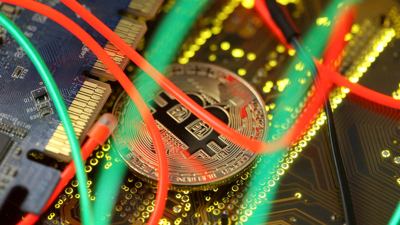 A gold coin emblazoned with the bitcoin symbol sits among wires and circuitboards.