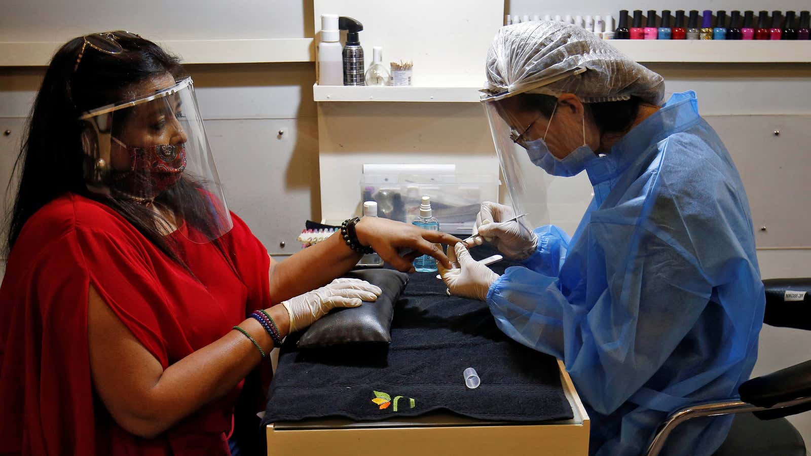 A beautician wearing protective gear tends to a customer wearing a protective face shield inside a parlor at a shopping mall after authorities allowed reopening…